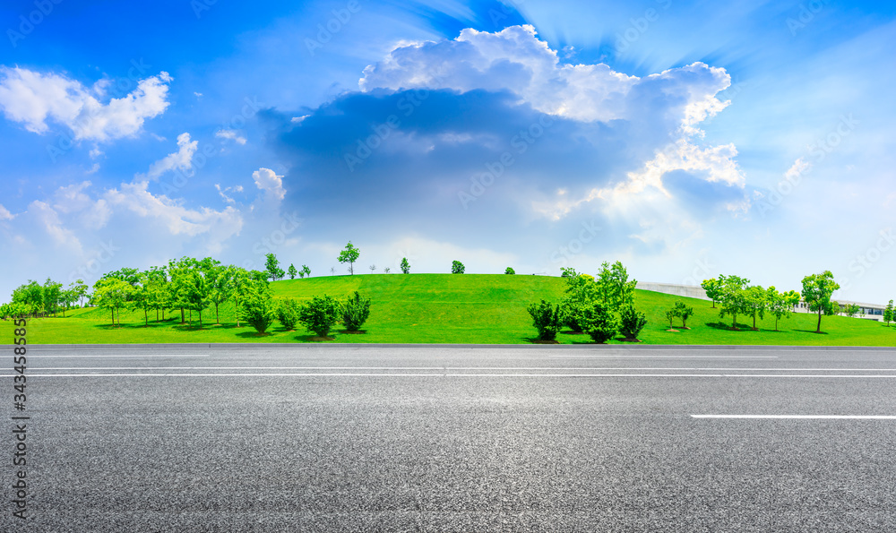 Empty asphalt road and green grass with tree under the blue sky.