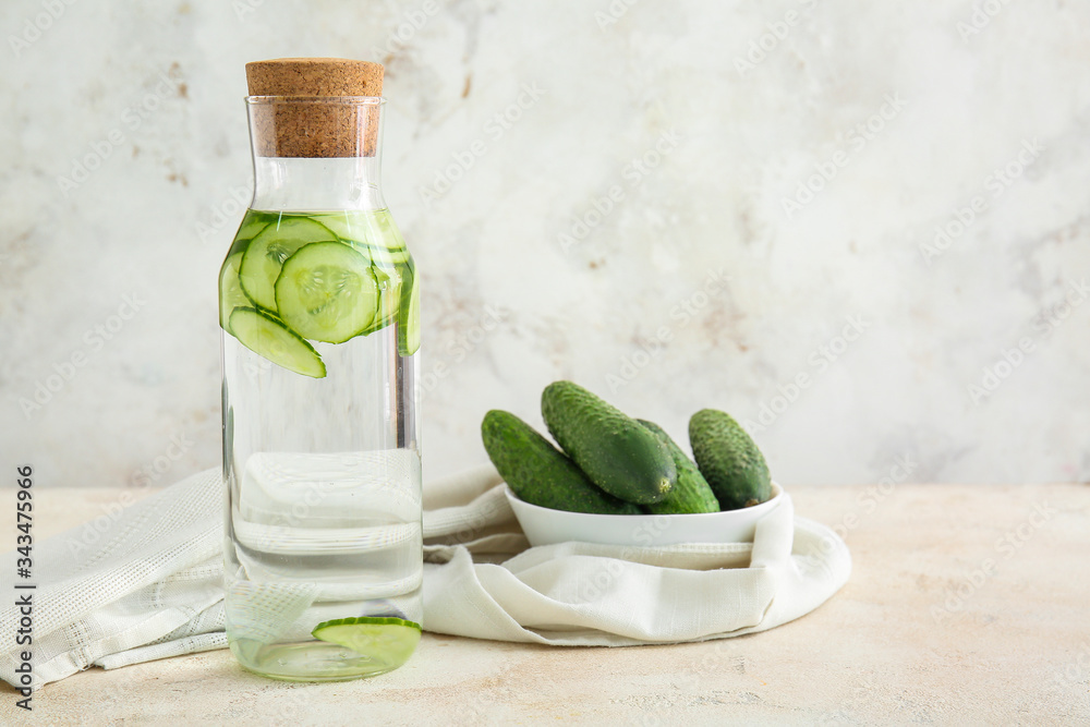 Bottle of infused cucumber water on light background