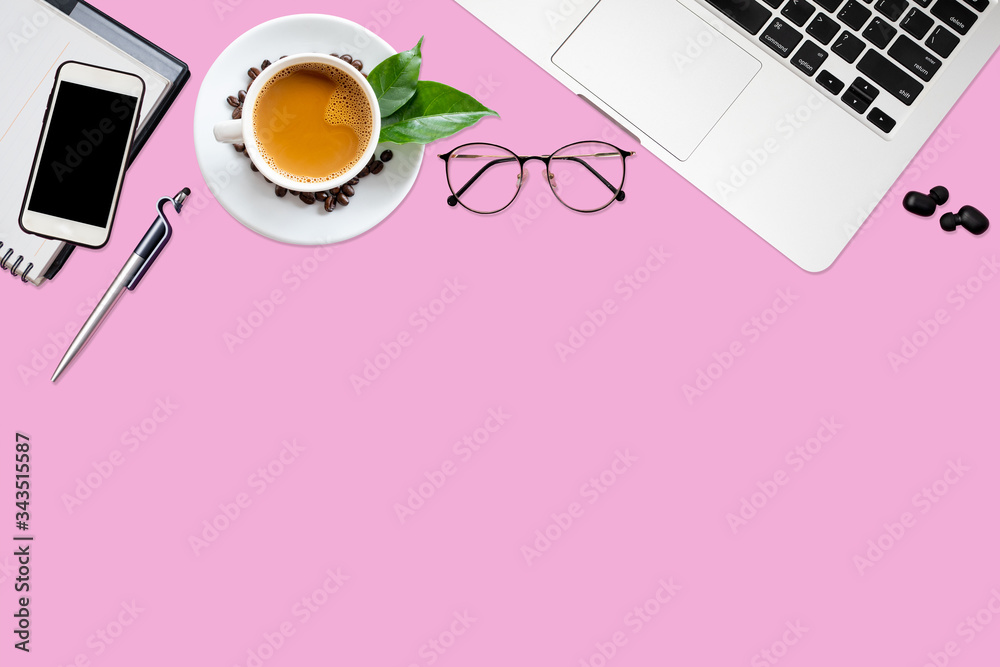 Top view of pink office desk table with laptop, smartphone, coffee cup, notebook, glasses with copy 