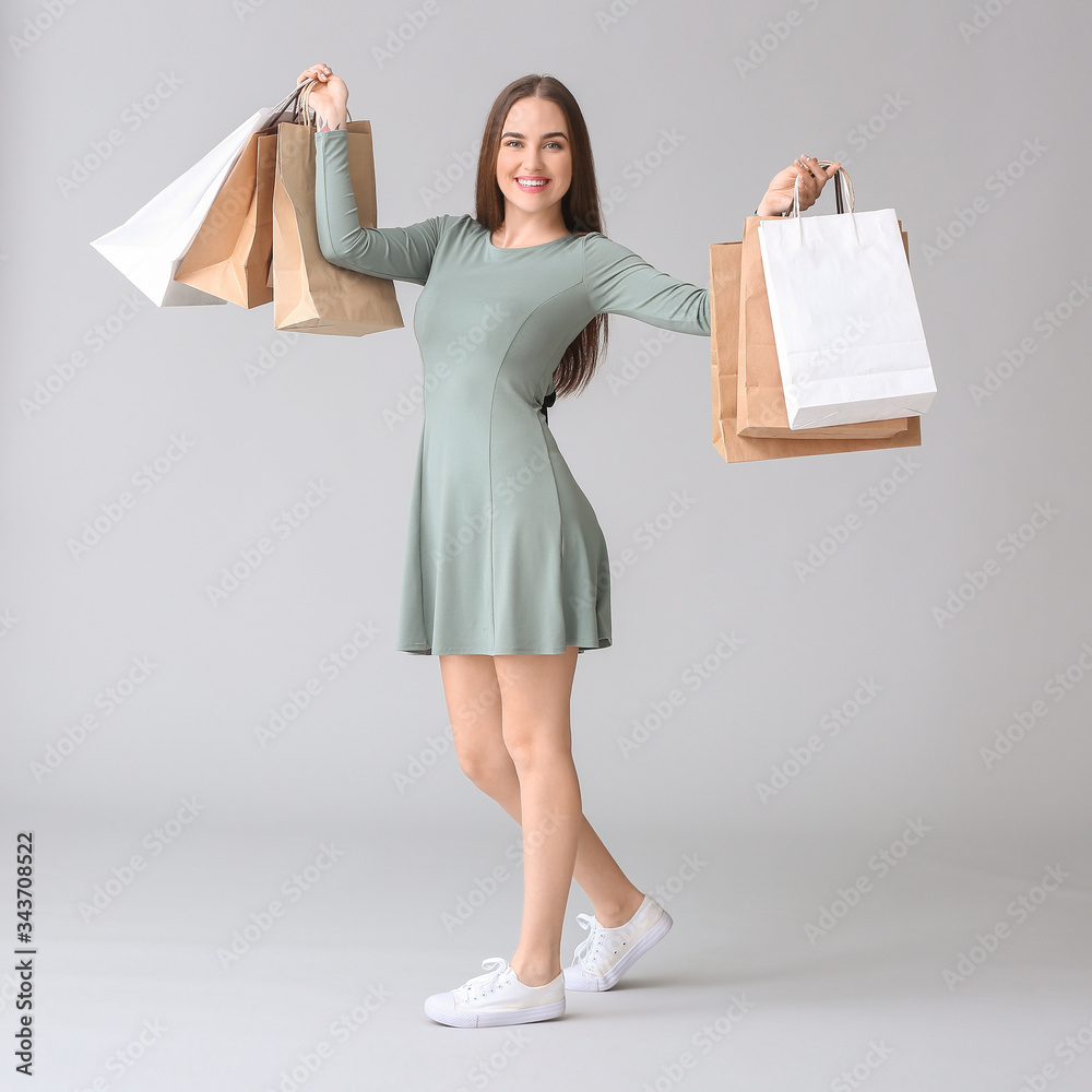 Young woman with shopping bags on grey background