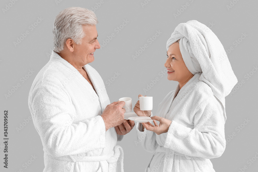 Mature couple in bathrobes drinking coffee on grey background