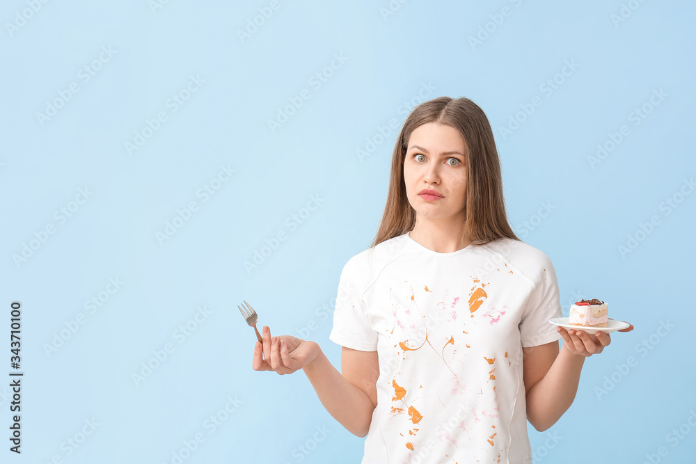 Troubled woman in dirty clothes eating dessert on color background