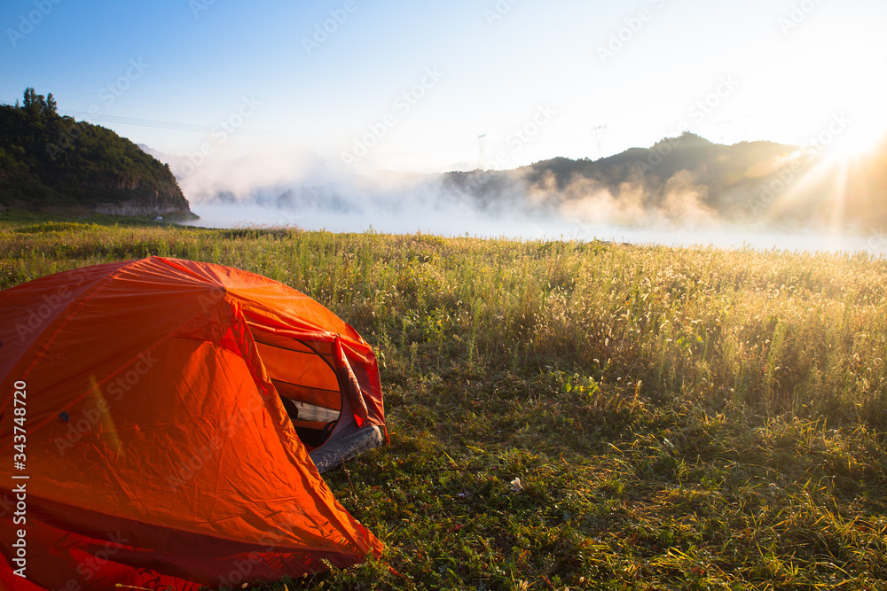 Camping tent by a lake with mist at sunrise