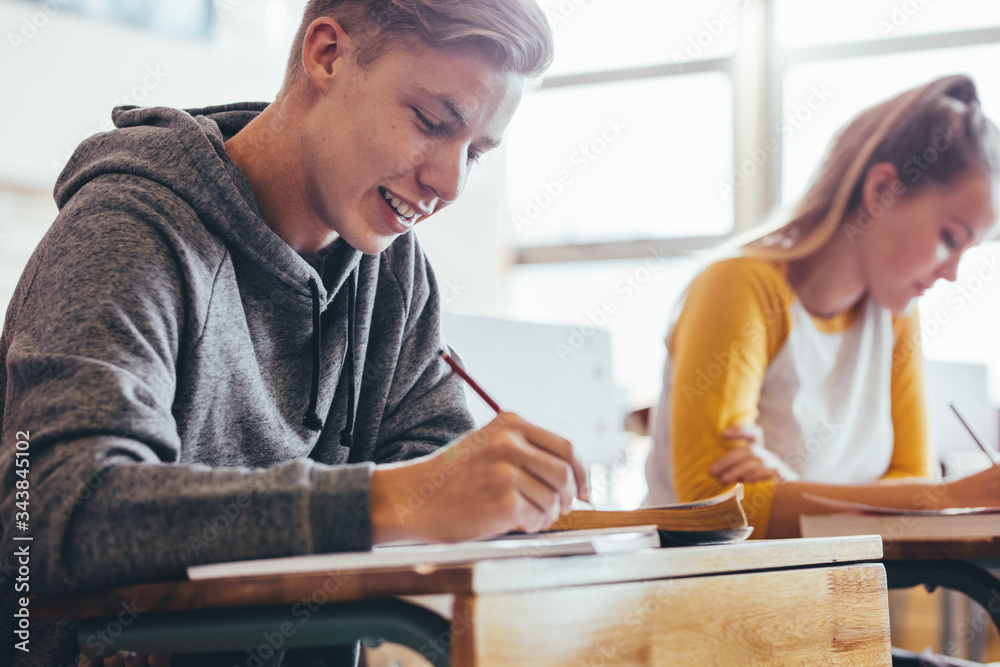 Teenage boy sitting in high school classroom writing in book