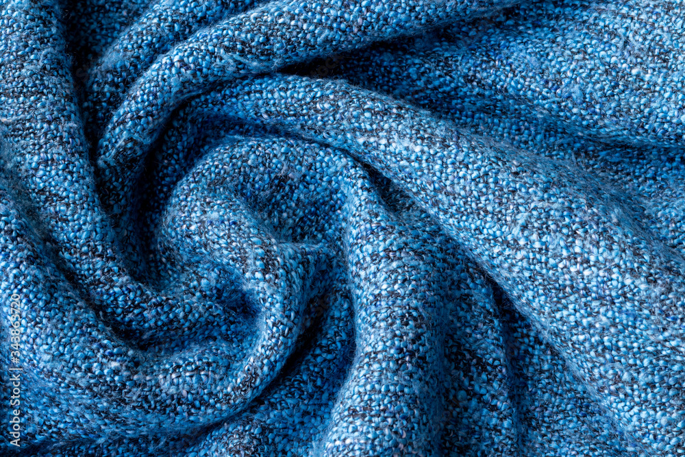 Bright blue knitted fabric texture. Crumpled twisted blanket background. Selective focus. Closeup vi