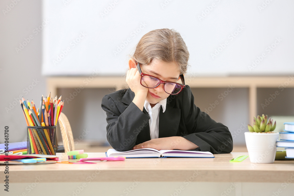 Bored little schoolgirl at desk in classroom