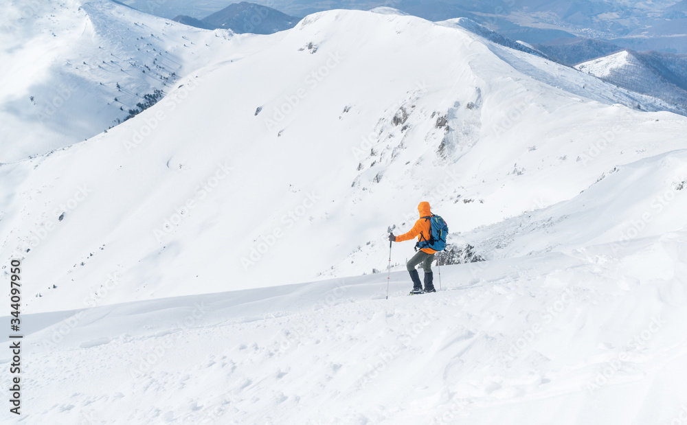 高山登山者穿着亮橙色软壳夹克，用登山杖从雪地上下来