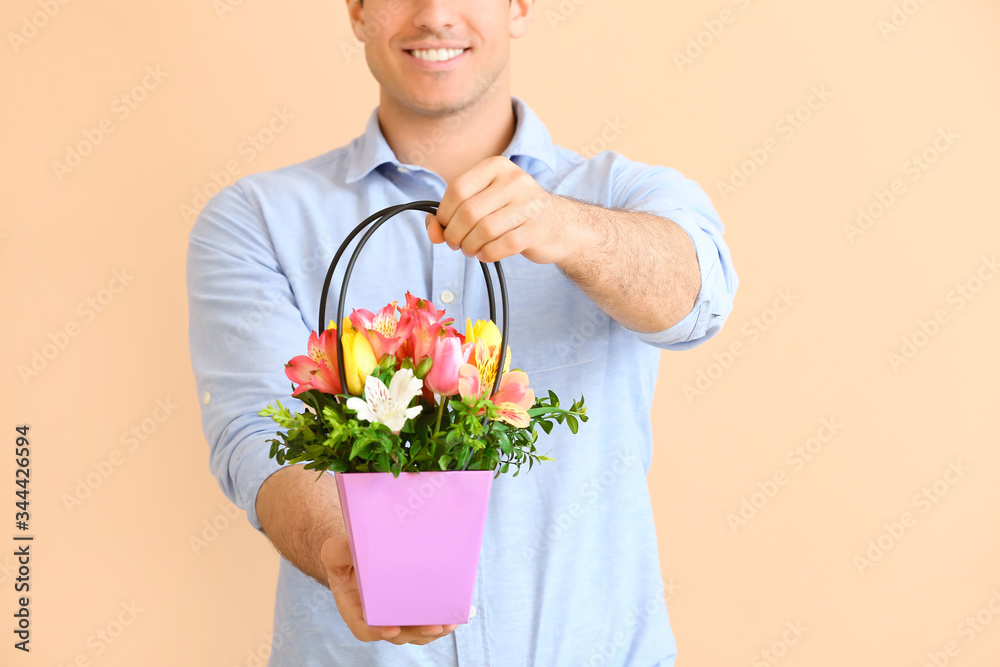 Handsome man with bouquet of flowers on color background