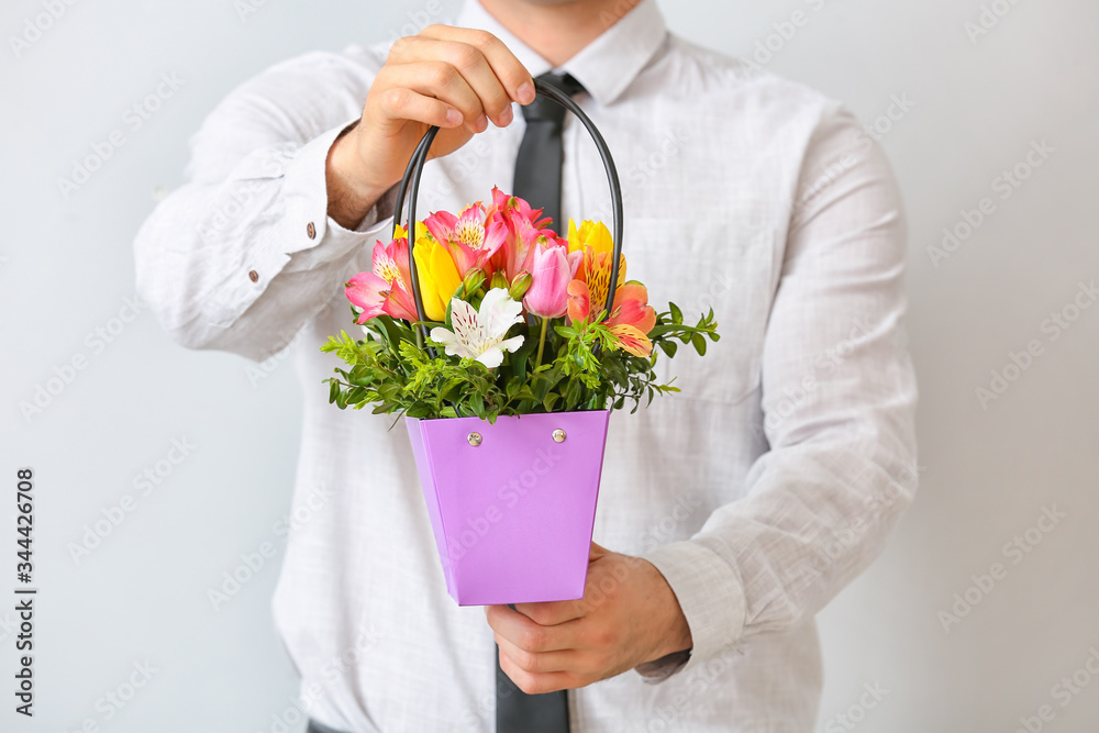 Handsome man with bouquet of flowers on light background