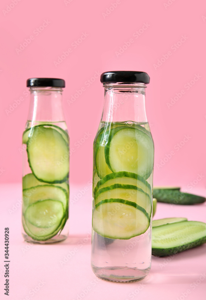 Bottles of cucumber infused water on color background