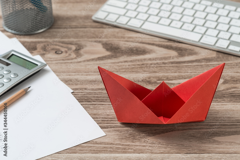 Businessman workspace at desk with red paper ship