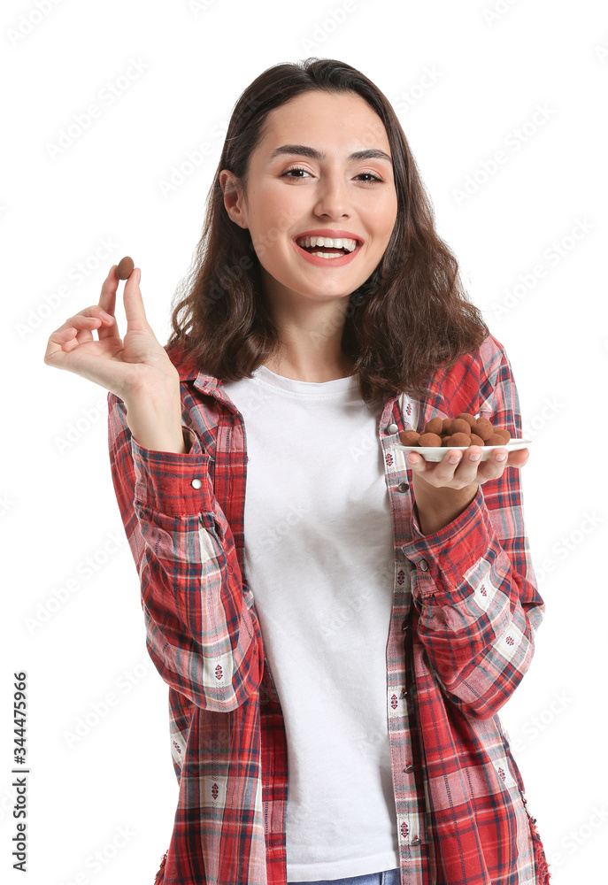 Beautiful young woman eating tasty chocolate candies on white background