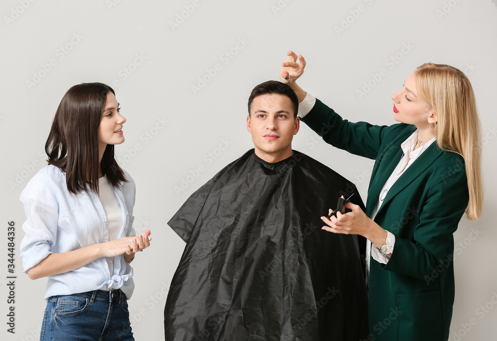 Young hairdressers working with client against light background