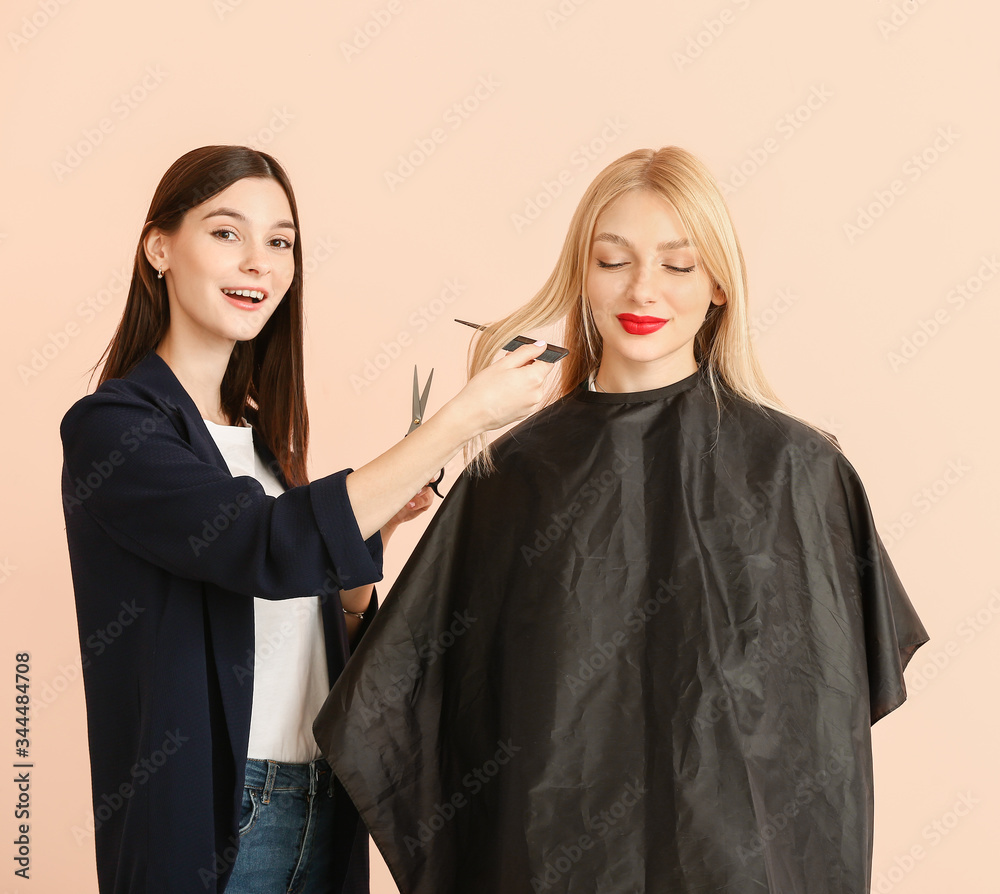 Young hairdresser working with client against color background