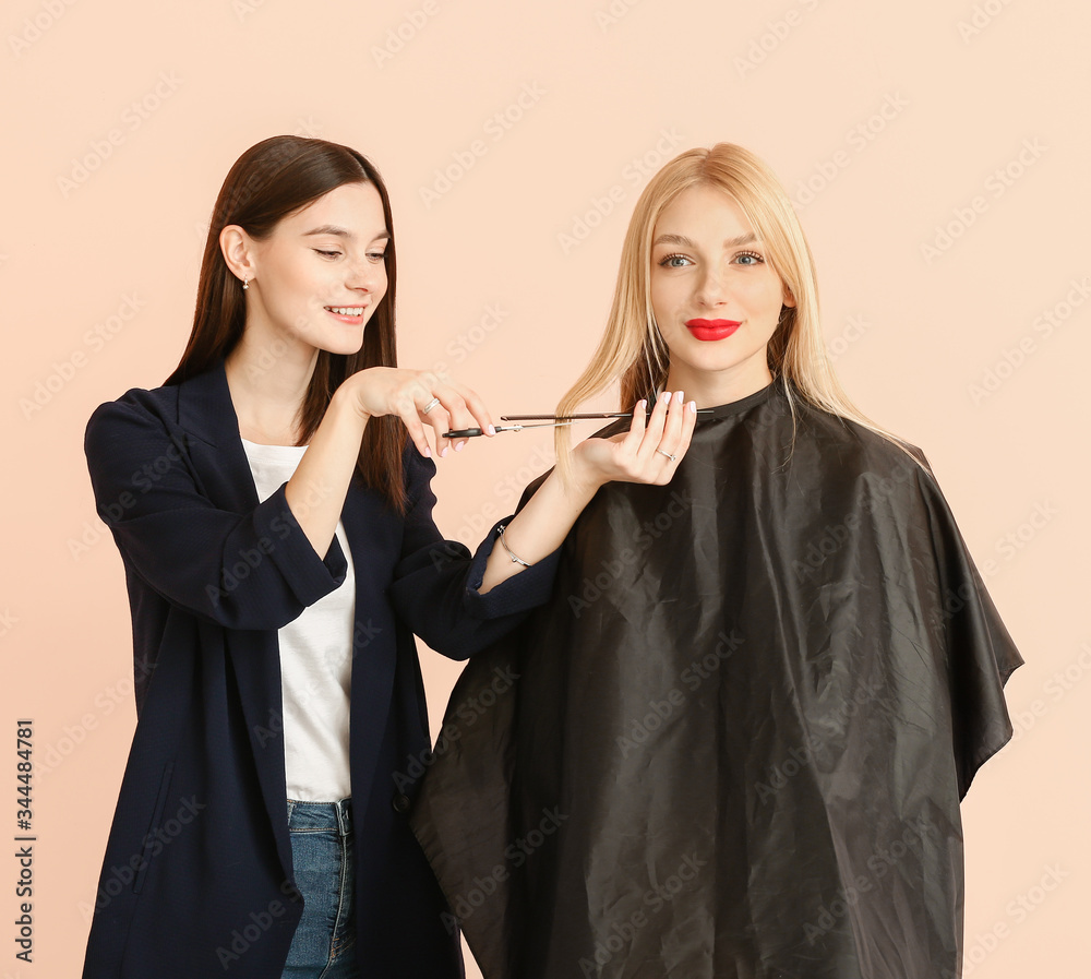 Young hairdresser working with client against color background