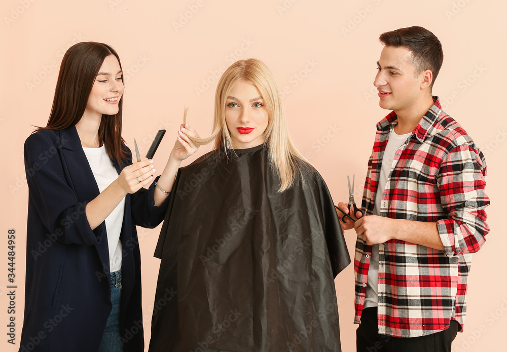 Young hairdressers working with client against color background