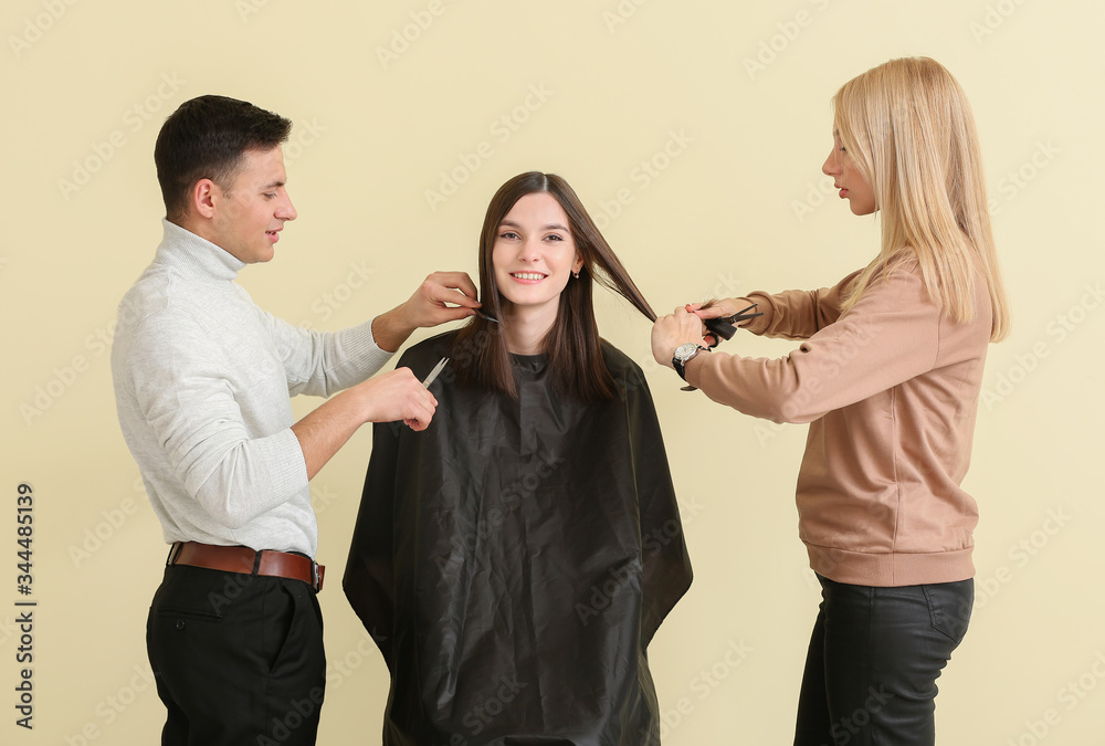 Young hairdressers working with client against color background