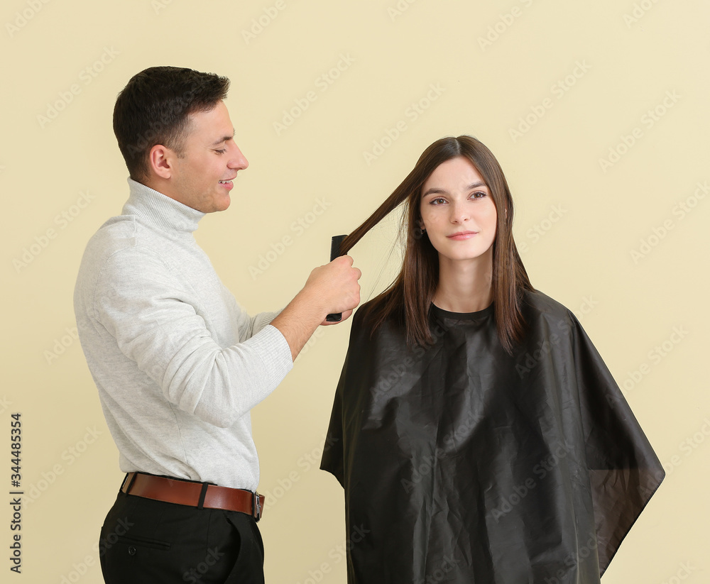 Young hairdresser working with client against color background