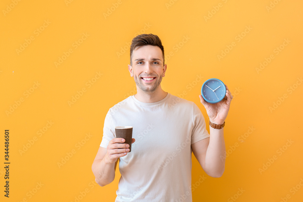 Young man with coffee and alarm clock on color background