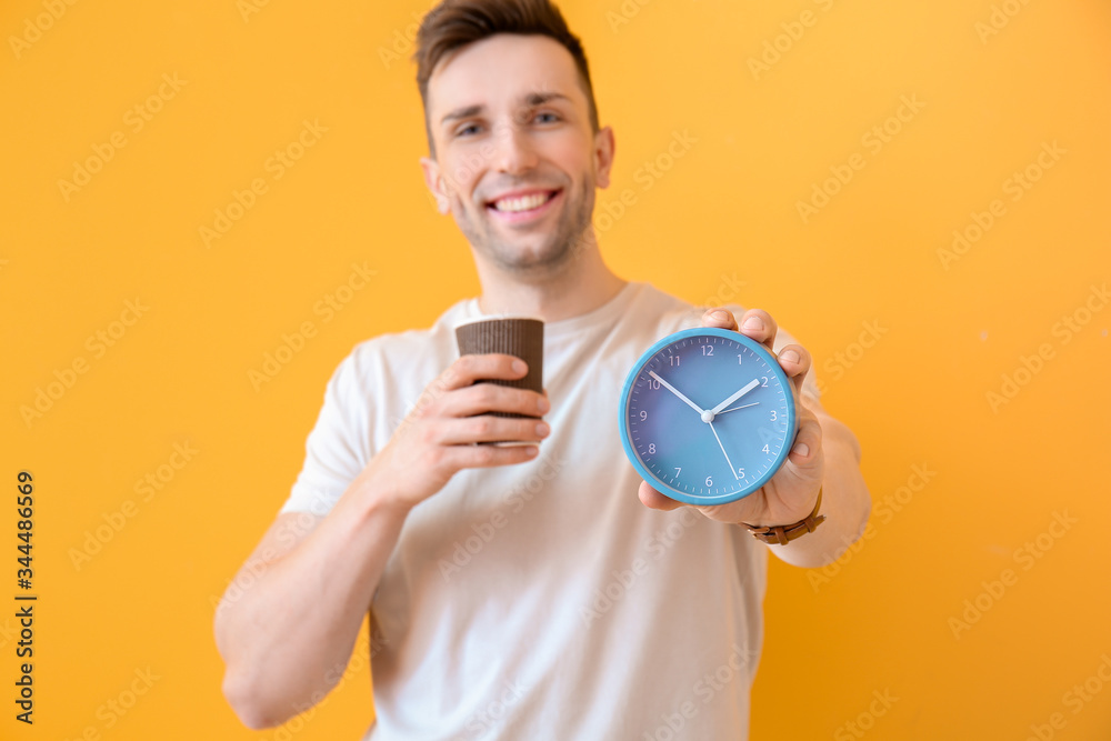 Young man with coffee and alarm clock on color background