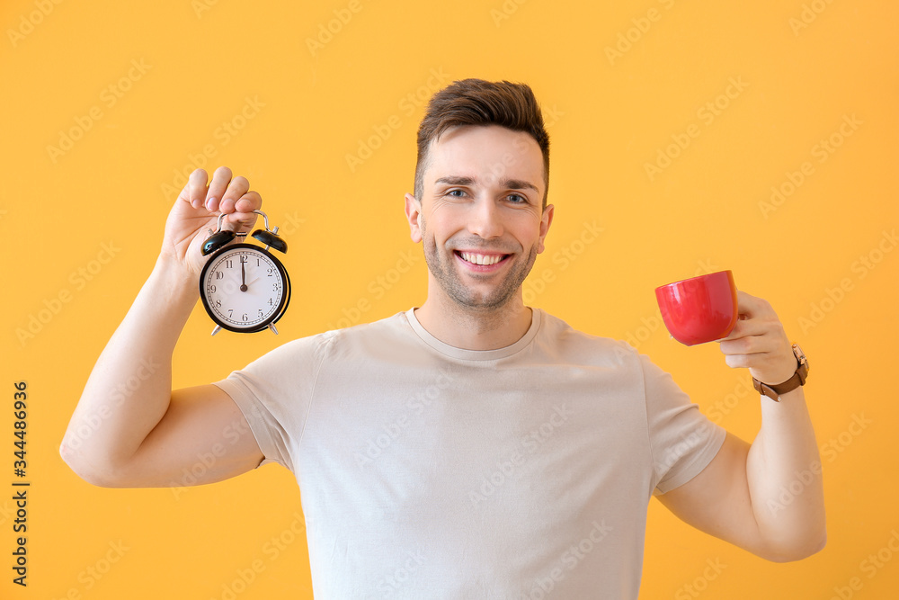 Young man with coffee and alarm clock on color background