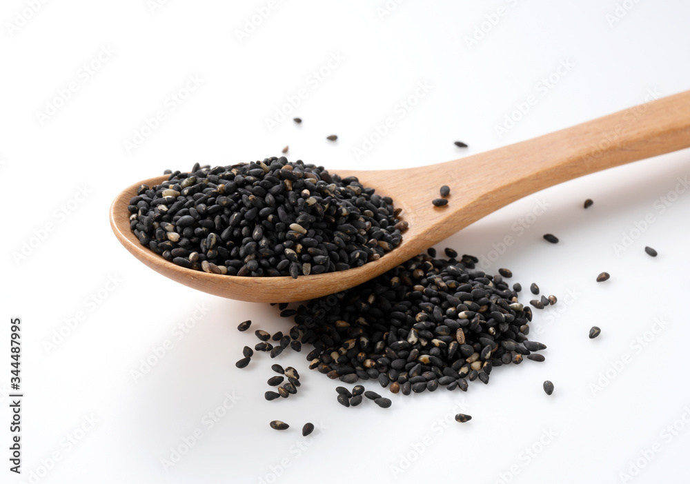 Black sesame seeds in a wooden spoon placed on a white background