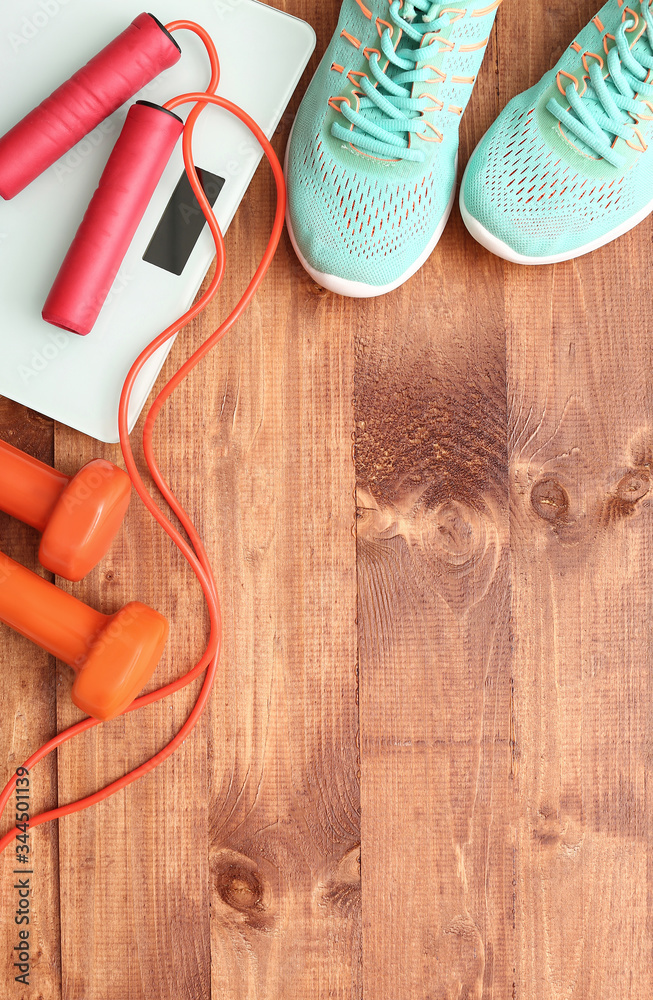 Sport shoes, dumbbells, jumping rope and weight scales on wooden background