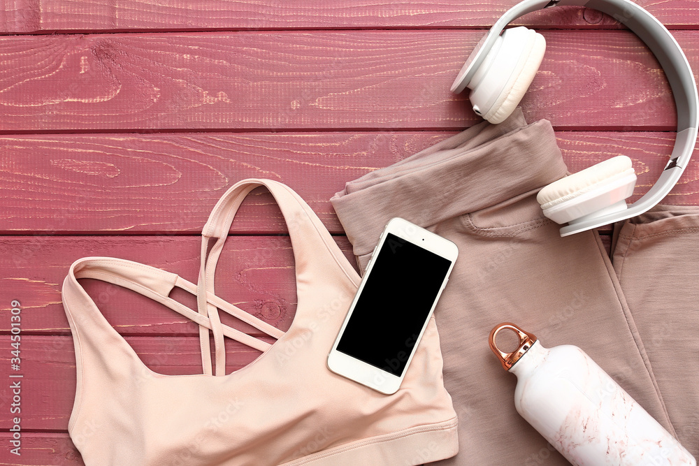 Sportswear, mobile phone, headphones and bottle of water on wooden background