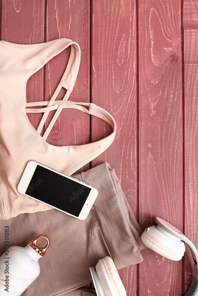 Sportswear, mobile phone, headphones and bottle of water on wooden background