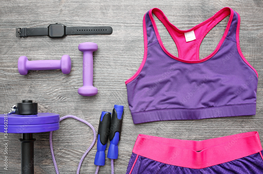 Sportswear, dumbbells, jumping rope and fitness tracker on wooden background