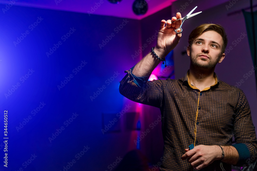 Professional hairdresser with scissors. Dark stylish background. Man wearing shirt. Looking aside an