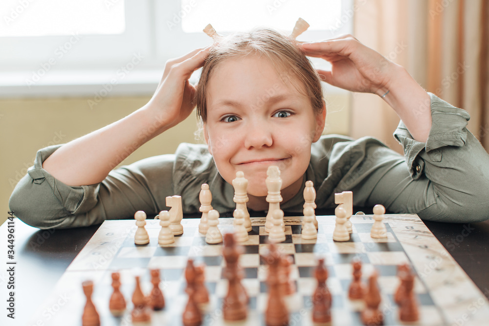 the girl is playing chess at the table and smiling . Board games, development of children in quarant