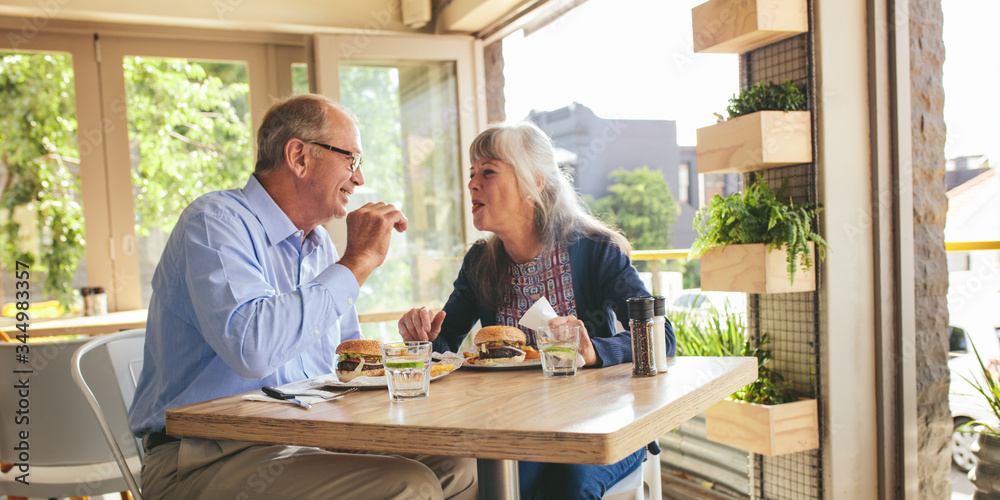 Senior couple enjoying eating burger together at a cafe