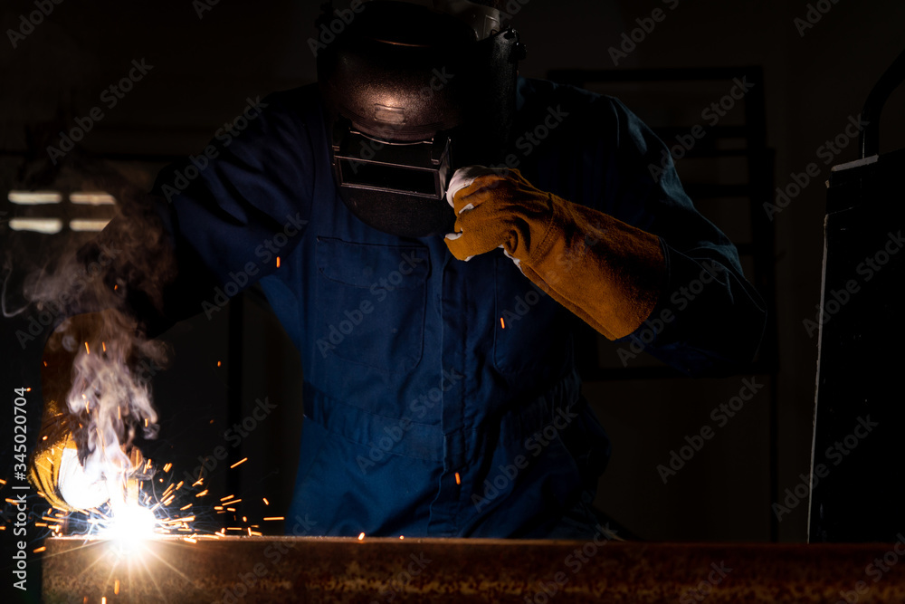 Metal welder working with arc welding machine to weld steel at factory while wearing safety equipmen