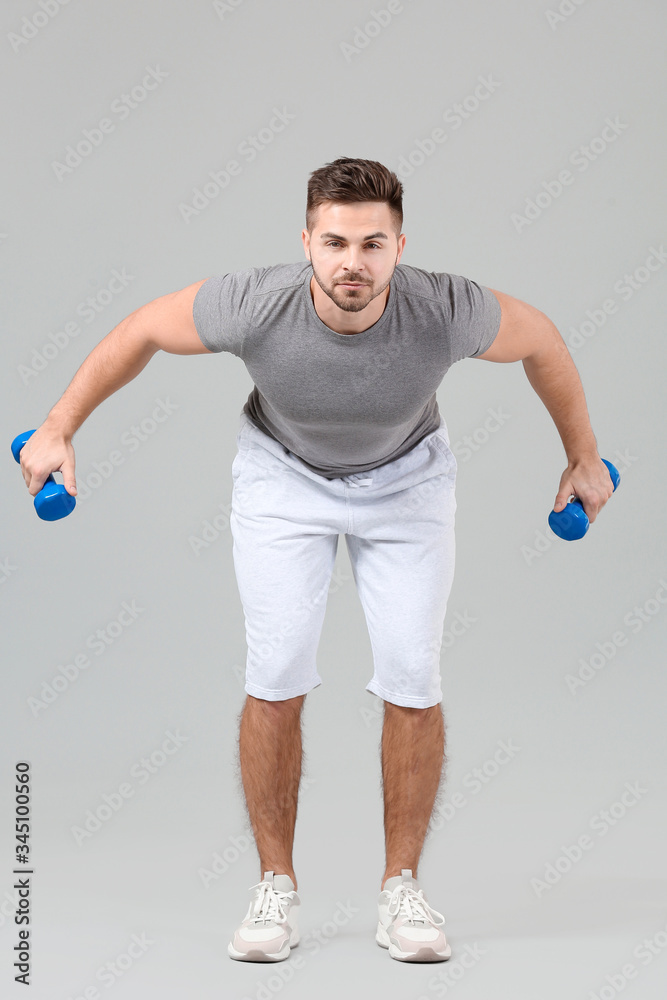 Sporty young man training with dumbbells on grey background