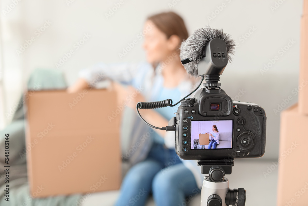 Young female blogger recording video while unpacking parcel at home