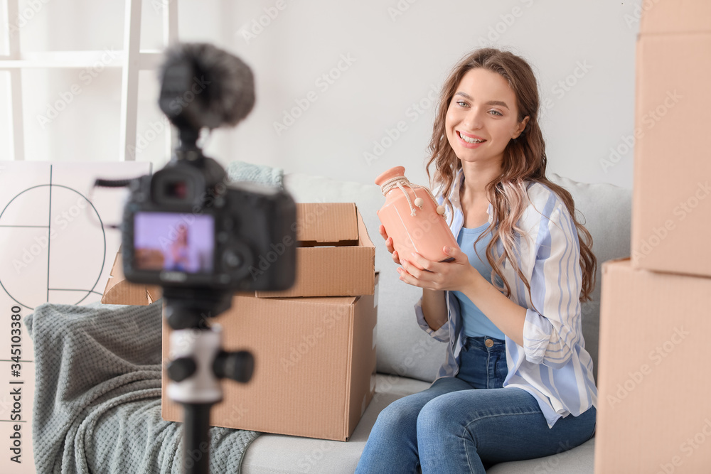 Young female blogger recording video while unpacking parcel at home