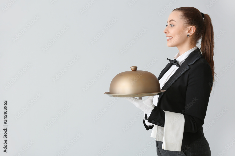 Female waiter with tray and cloche on grey background