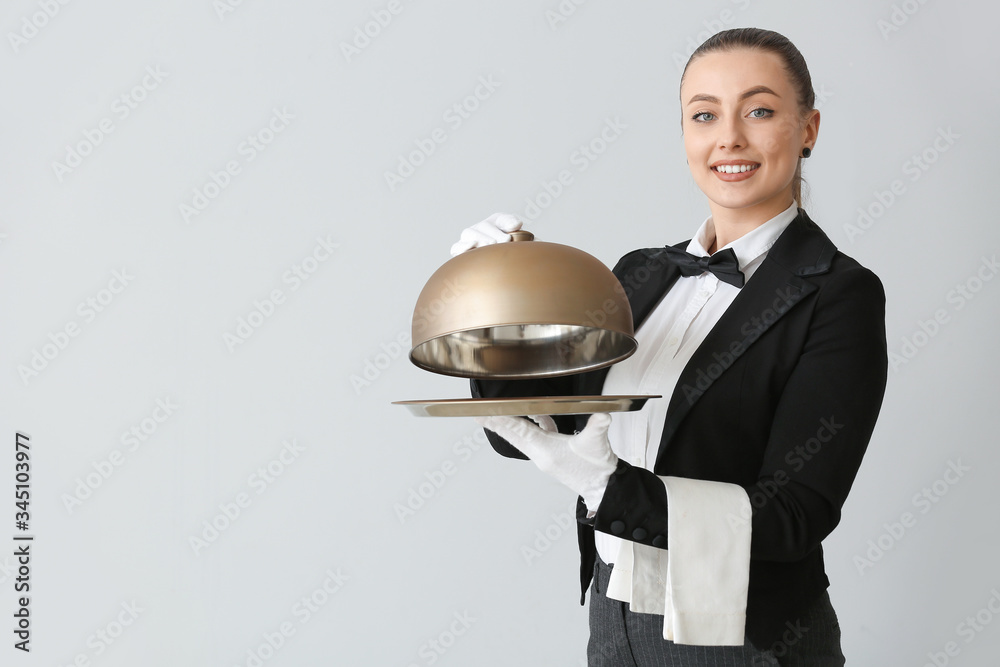 Female waiter with tray and cloche on grey background