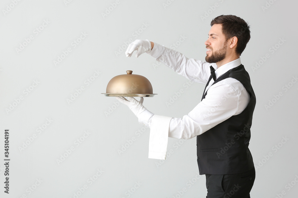 Male waiter with tray and cloche on grey background