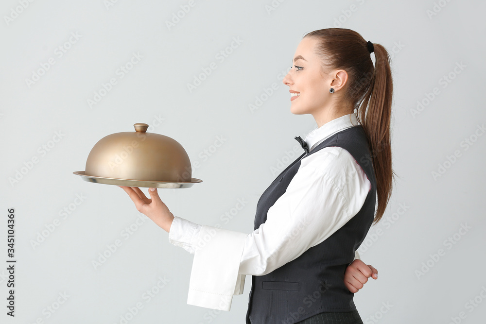 Beautiful female waiter with tray and cloche on grey background