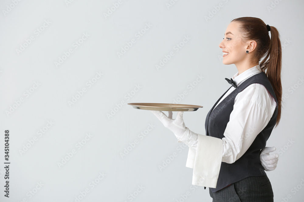 Beautiful female waiter with empty tray on grey background