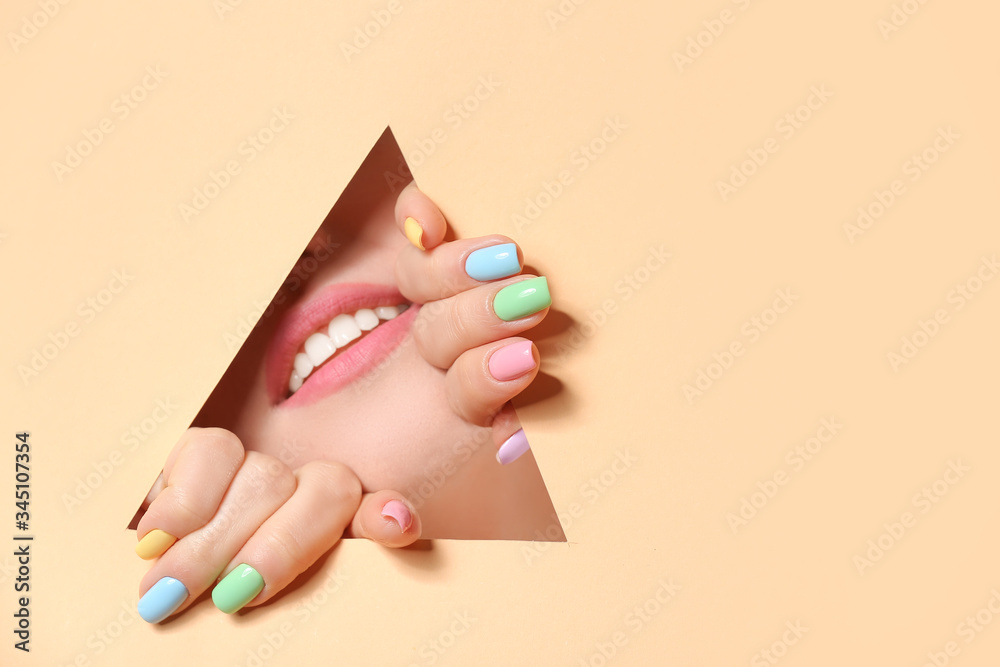 Young woman with beautiful manicure visible through cut color paper