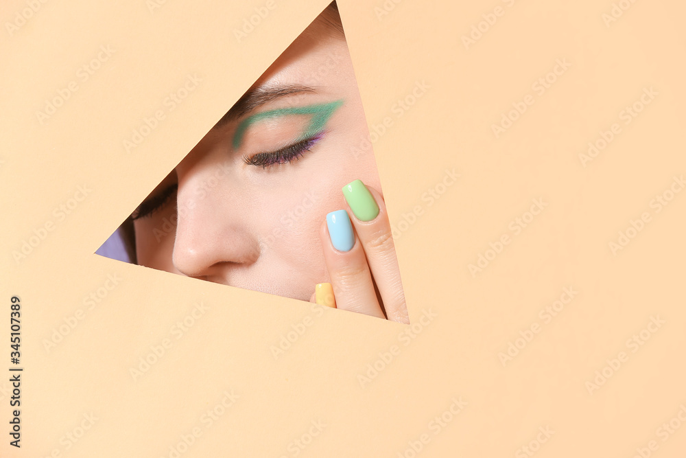 Young woman with beautiful manicure visible through cut color paper