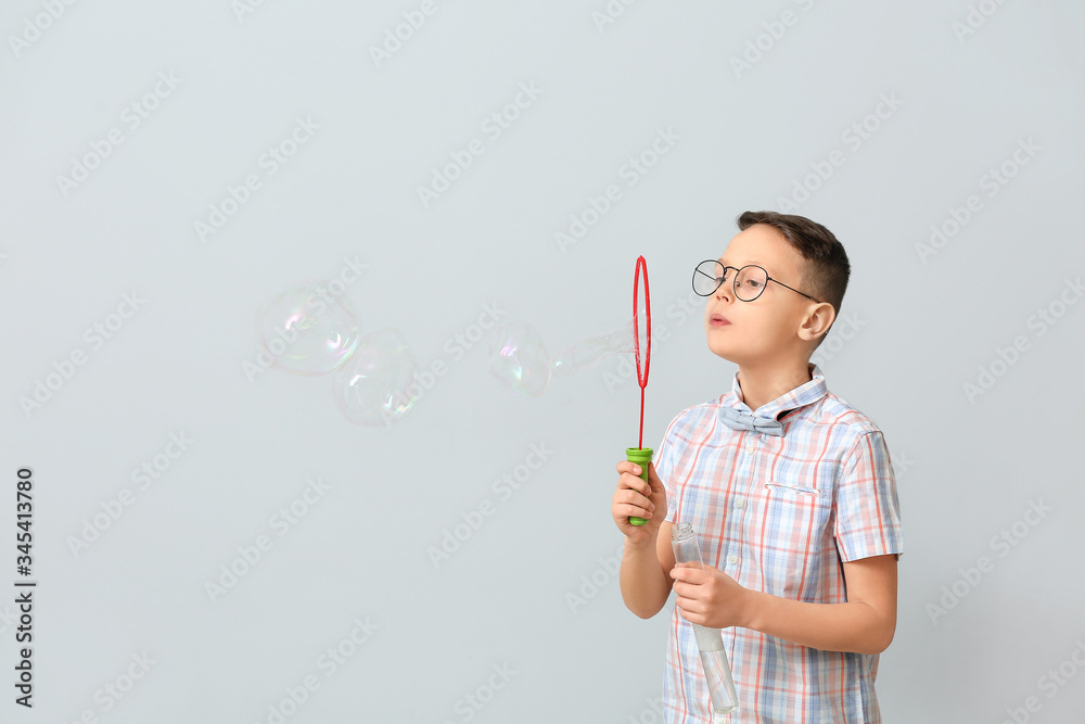 Cute little boy blowing soap bubbles on light background