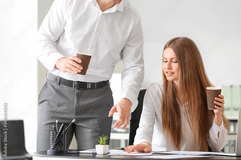 Young colleagues drinking coffee while working in office