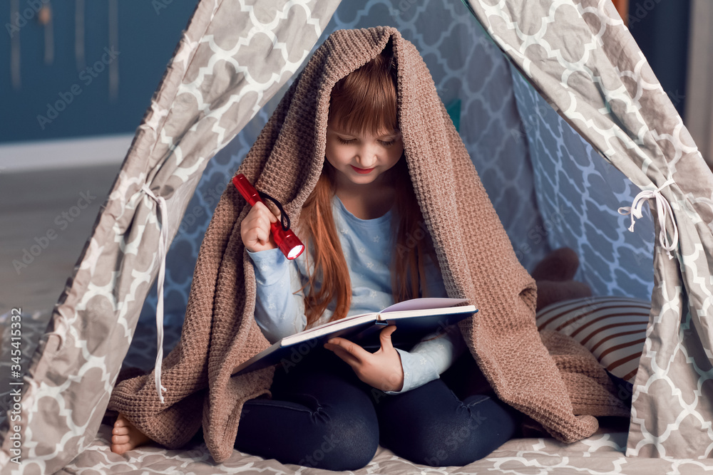 Little girl reading book in play tent at night