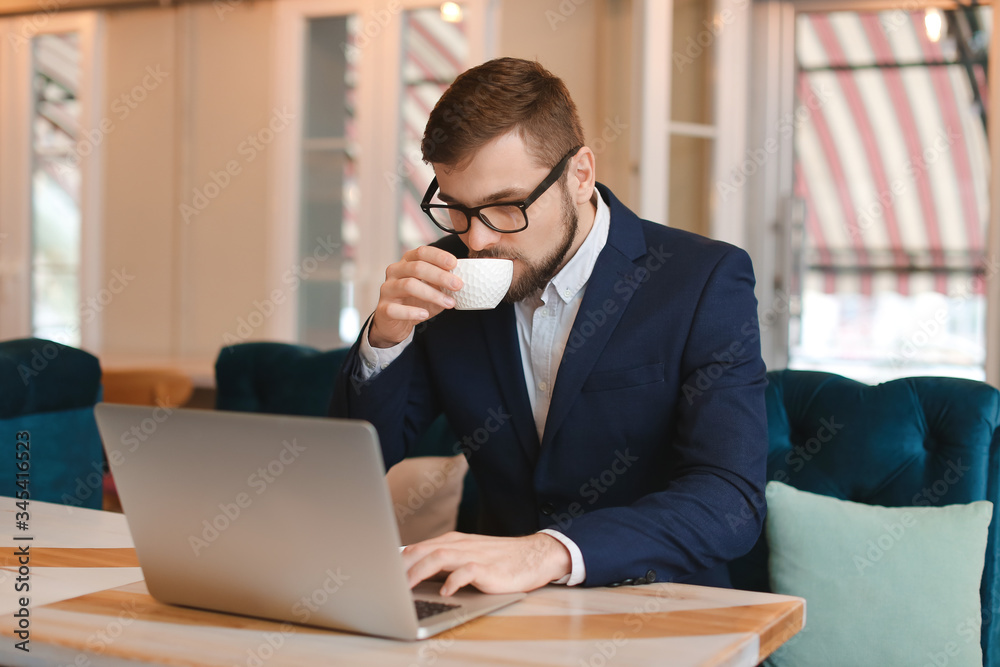 Young businessman drinking coffee during work in cafe