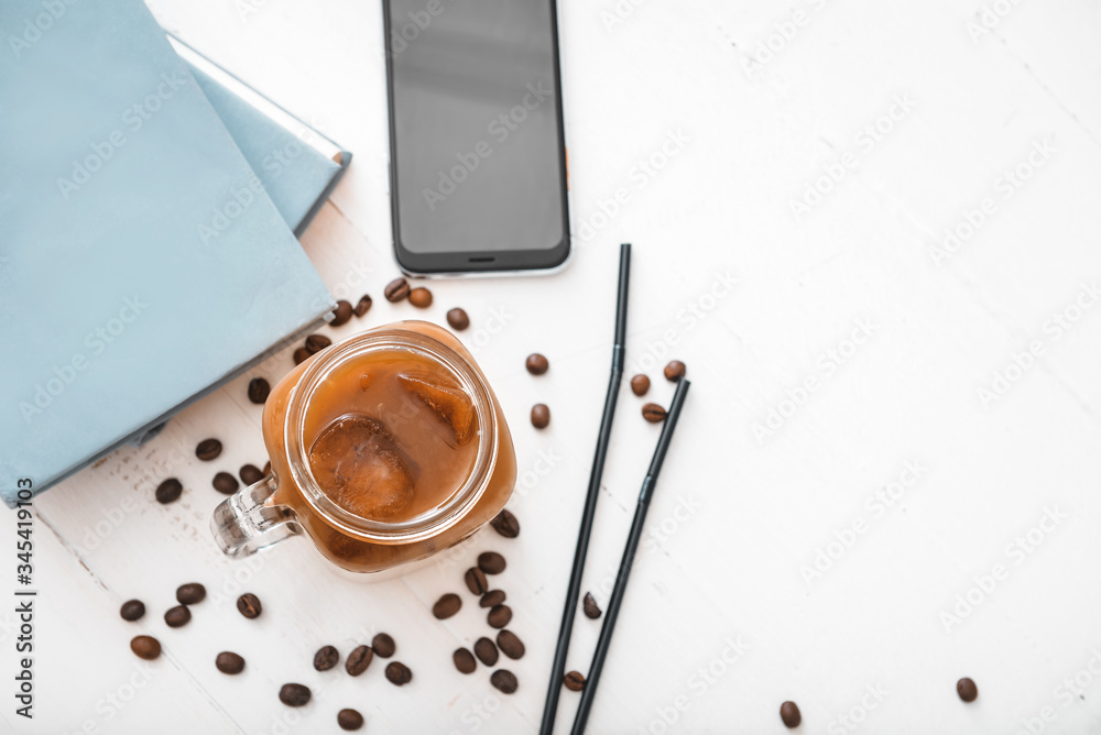 Mason jar of tasty iced coffee with notebooks and mobile phone on table