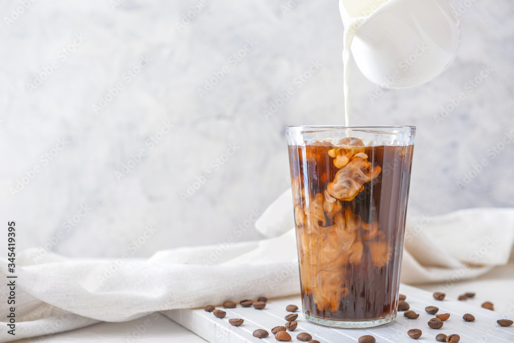 Pouring of milk into cold coffee in glass on table